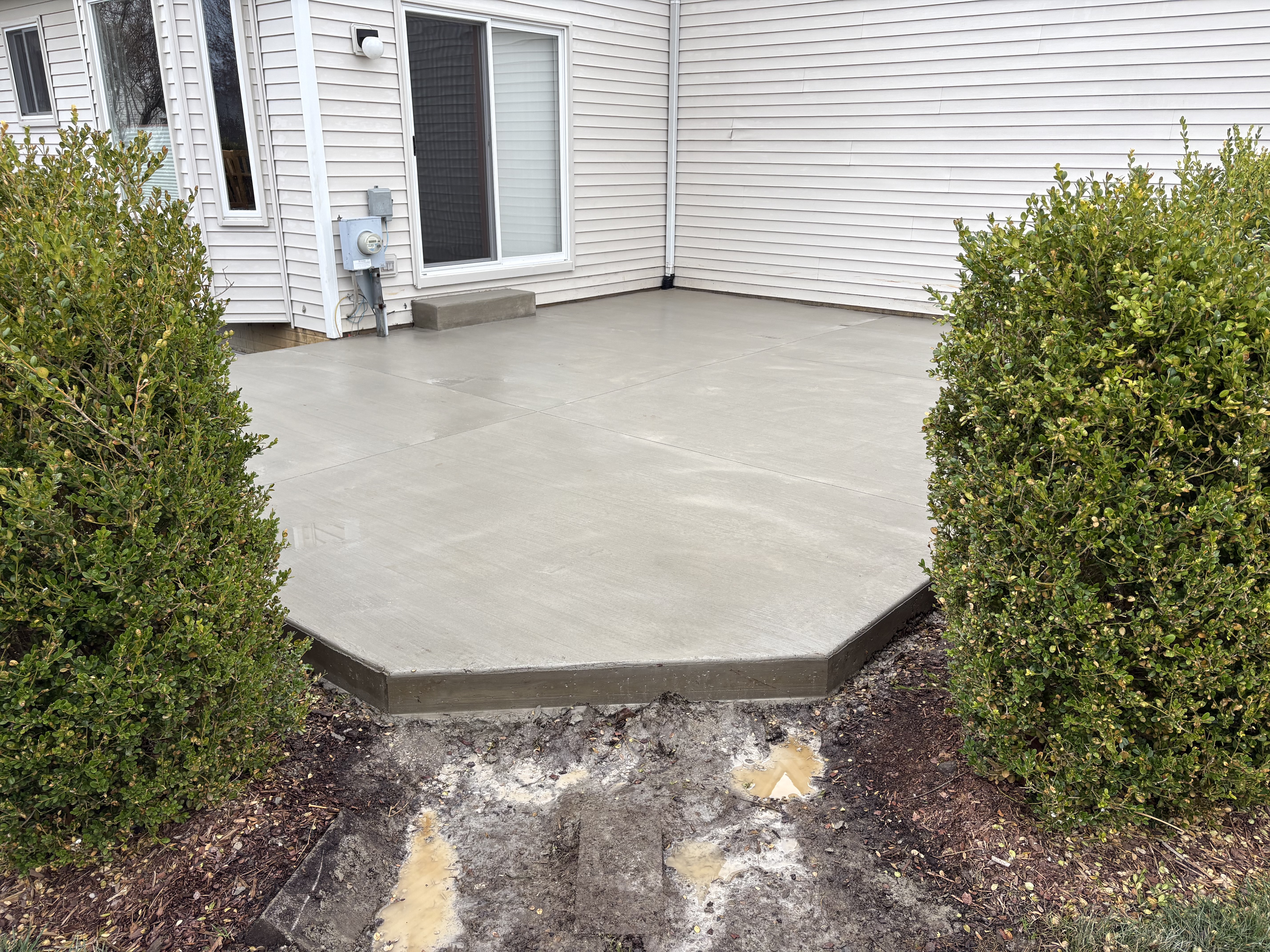 Custom-shaped concrete patio with smooth finish between hedges