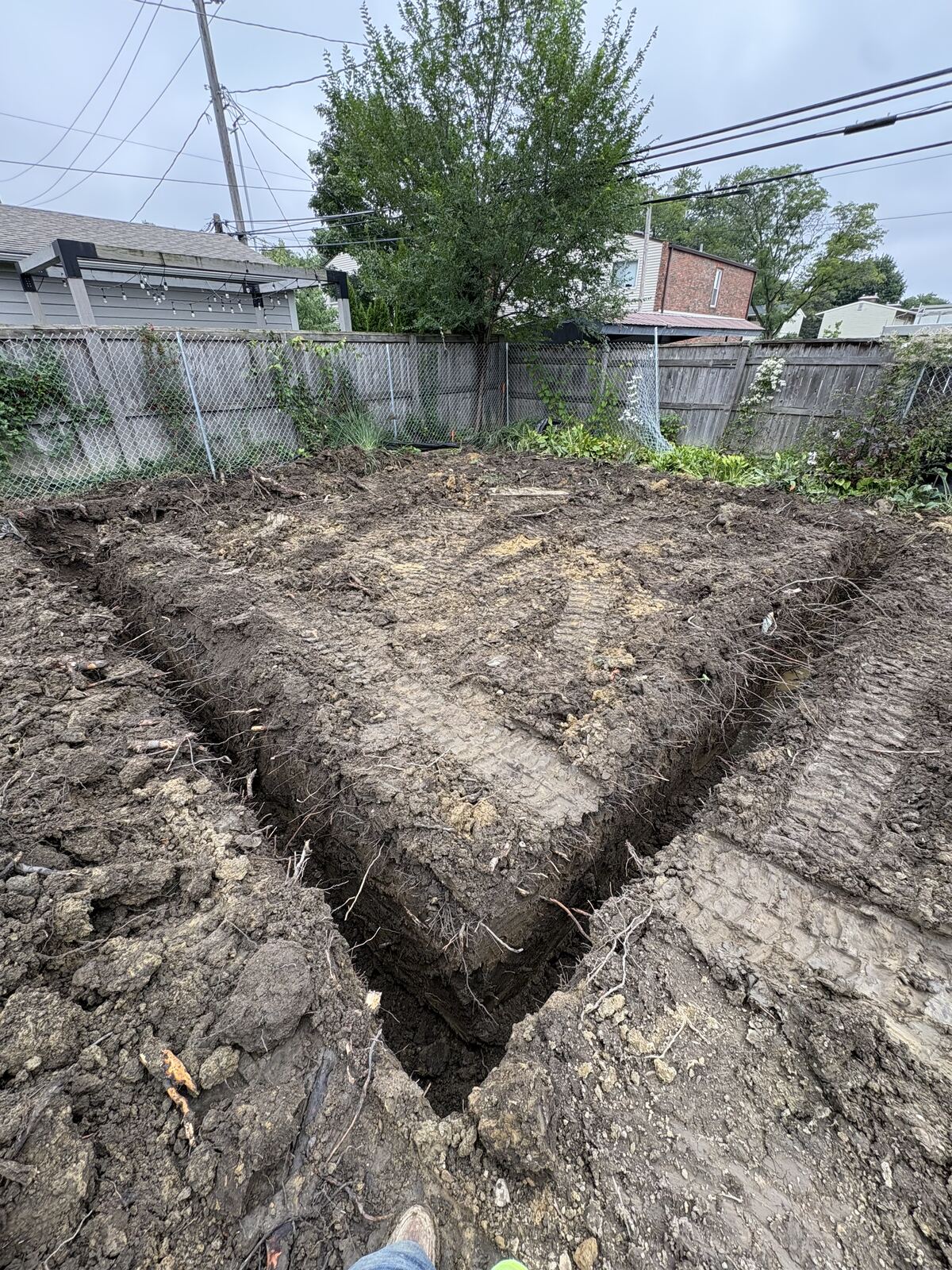 Excavated footing trenches for a new foundation in a fenced backyard